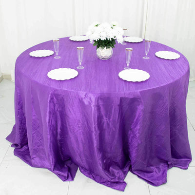 Purple tablecloth draped over a round table set with plates and glasses.