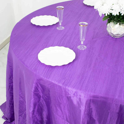 Purple tablecloth on a round table with white plates and glasses.