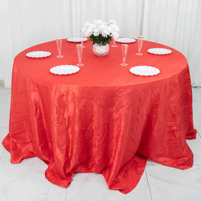 Red tablecloth draped over a round table set with white plates and a floral centerpiece.