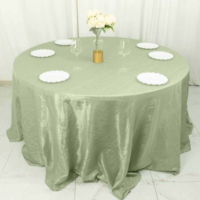 Round olive green tablecloth draped over a table with plates and glasses.