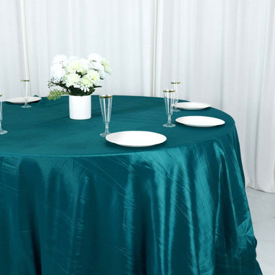 Teal satin tablecloth with white plates and floral centerpiece on a round table.