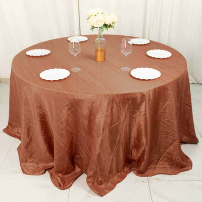 Round brown tablecloth draped over a table set for dining with plates and glasses.
