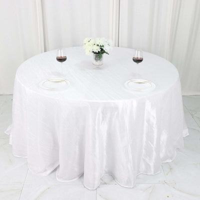 Round dining table set with wine glasses and flowers on a white tablecloth.