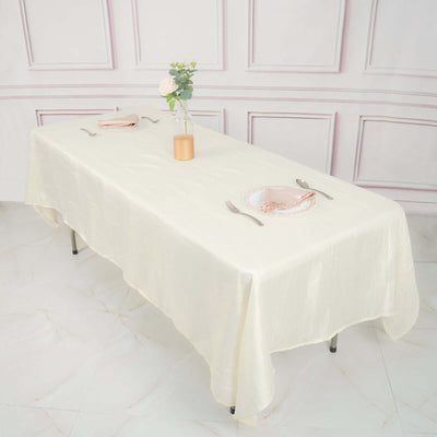 Elegant cream tablecloth draped over a dining table with plates and a vase.