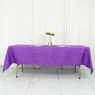Purple tablecloth draped over a table set for dining with flowers and glasses.