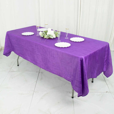 Purple tablecloth draped over a table set for an event with white plates and decorations.