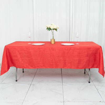 Red tablecloth draped over a dining table set for two with glasses and a floral centerpiece.