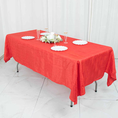 Red tablecloth draped over a table set for a gathering with plates and glasses.