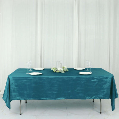 Teal satin tablecloth on a dining table set with plates and glassware.
