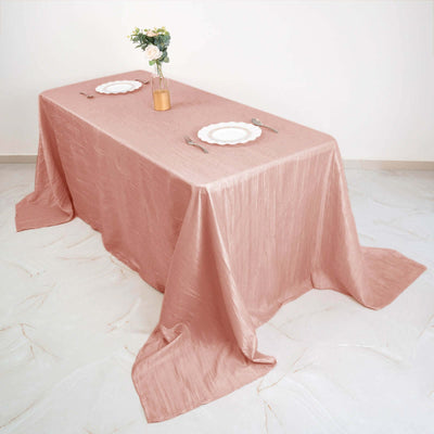 Elegant pink tablecloth draped over a table with plates and a vase.