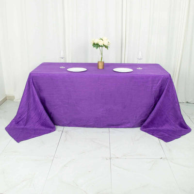 Purple tablecloth draped over a table set for two with plates and flowers.