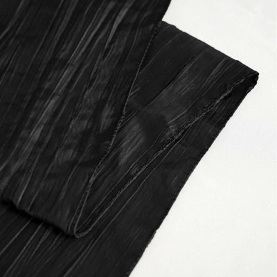 Black textured fabric draped elegantly on a plain backdrop.