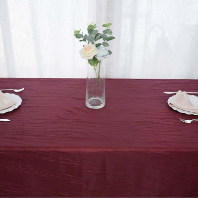 Elegant burgundy tablecloth with a vase of flowers and plates set for a meal.