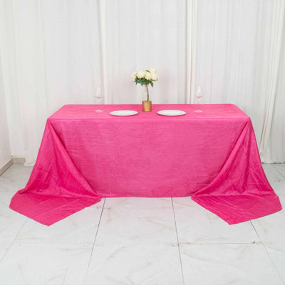 Pink tablecloth draped over a table with plates and flowers.
