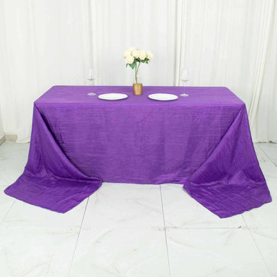 Purple tablecloth draped over a table with white plates and wine glasses.