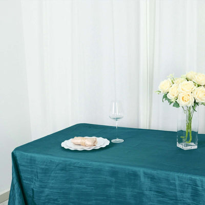 Teal tablecloth with a plate, glass, and vase of roses on a table.