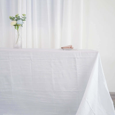 White tablecloth draped over a table with a vase and flower on top.
