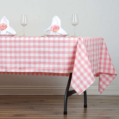 Pink gingham tablecloth draped over a table with wine glasses and napkins.