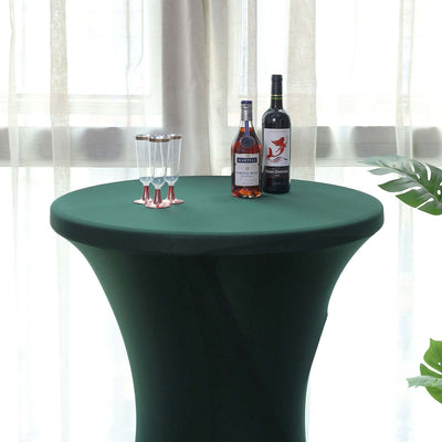 Green tablecloth draped over a round table with drinks and glasses on top.