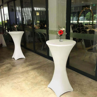 Two white cocktail tables with flower vases in a modern event space.