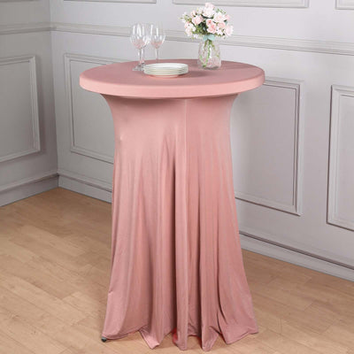 Pink table cover draped over a round table with glasses and flowers.