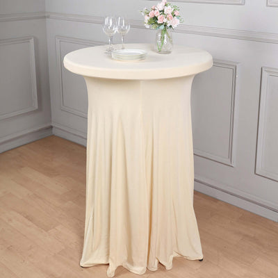 Cream-colored fitted table cover on a round table with glassware and flowers.