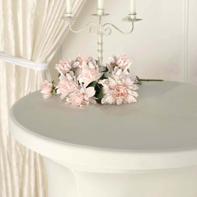 Pink artificial flowers on a white table with a candle holder.