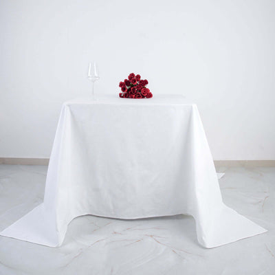 White tablecloth with a glass and bouquet of red roses on top.