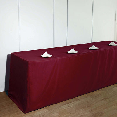 Maroon table cover with white plates on top, styled for a formal setting.
