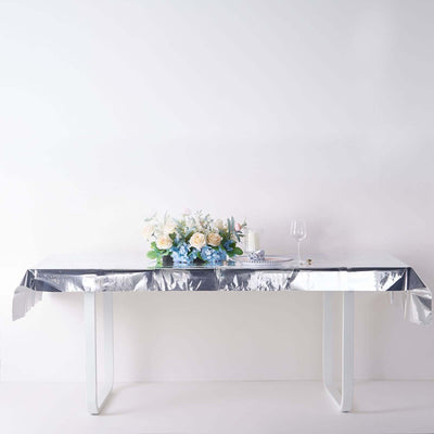 Silver tablecloth on a table adorned with flowers and a glass against a plain backdrop.