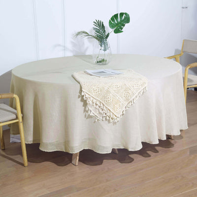 Round beige tablecloth draped over a table with a plant centerpiece.