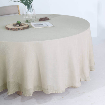 Round beige tablecloth draped over a table with a vase and decor.