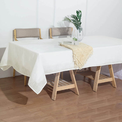 White tablecloth draped over a wooden table with a vase and decorative piece.