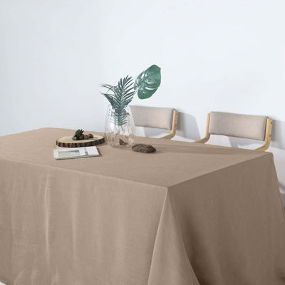 Beige linen tablecloth draped over a table with a vase and plants.