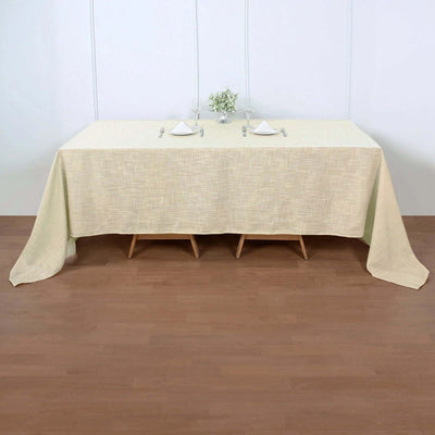 Beige textured tablecloth draped over a wooden table with elegant table setting.