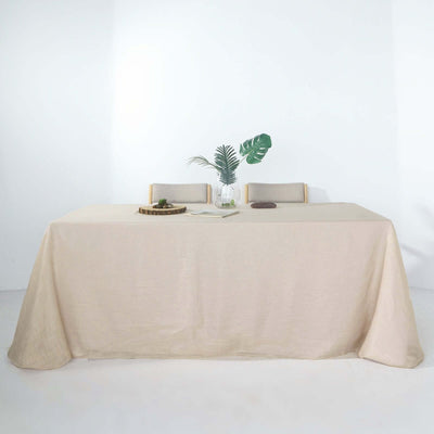 Beige tablecloth draped over a table with two chairs and a vase of greenery.