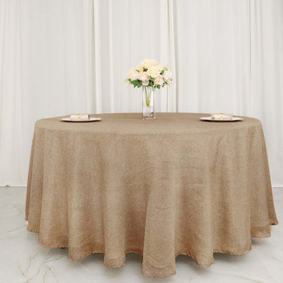 Round beige tablecloth draped over a table with flowers and plates.
