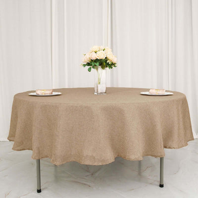 Round brown tablecloth draped over a table with plates and flowers.