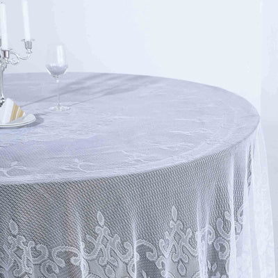 White lace tablecloth draped over a round table with a candle and glass.