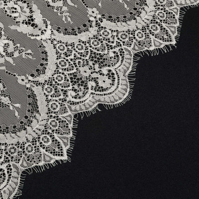 Intricate white lace fabric edge on a dark background.