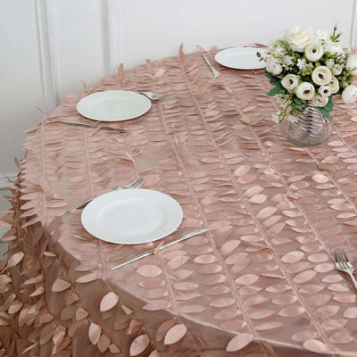 Round blush tablecloth with leaf design and white plates on a dining table.
