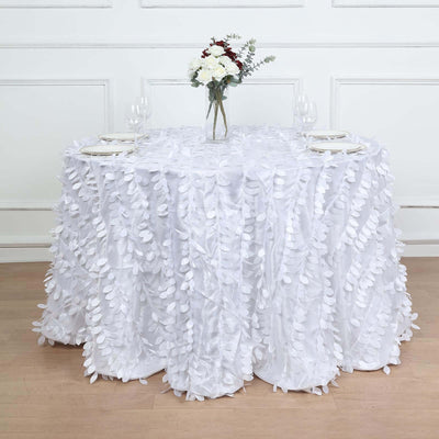 White table covered with leaf-patterned fabric, decorated with flowers and glassware.