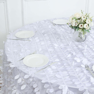 White tablecloth with leaf design, set for dining with plates and floral centerpiece.