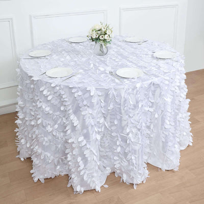 White tablecloth with textured leaf design on round table, set with plates and flowers.