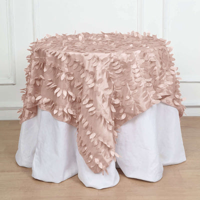 Blush pink tablecloth with leaf-shaped appliqués draped over a white table.
