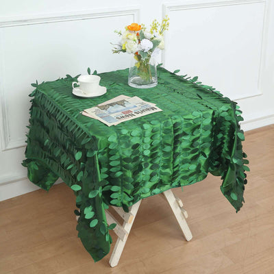 Green leaf-patterned tablecloth draped over a table with a vase and newspaper.