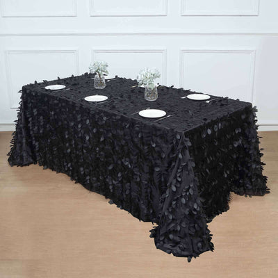 Black leaf-patterned tablecloth draped over a table with plates and flowers.