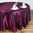 Burgundy tablecloth draped elegantly on a round table with dinnerware and napkins.