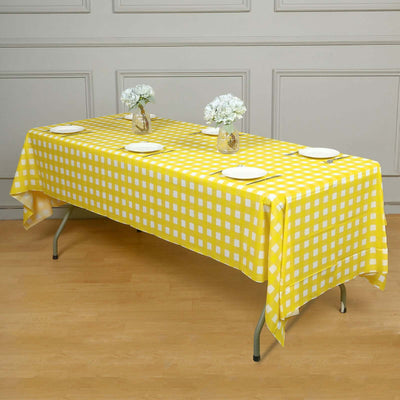 Yellow checkered tablecloth on a table with white plates and floral vases.