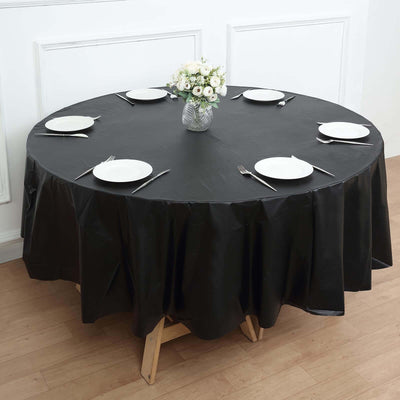 Black round tablecloth on a dining table set with plates and a flower vase.